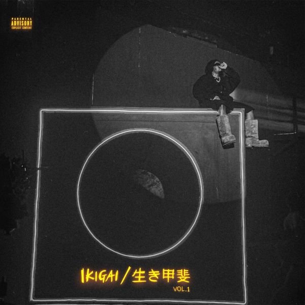 The cover art for the EP "Ikigai Vol. 1" by Olamide features a grayscale image with a dark, industrial background. A figure, likely the artist, is sitting on the edge of a large geometric structure, wearing rugged boots and a dark outfit. The title "IKIGAI / 生き甲斐 VOL. 1" is prominently displayed at the bottom in bright yellow text, with a parental advisory label in the top left corner.